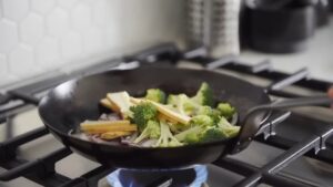 Broccoli, Tofu Strips, and Onions Being Stir-Fried in A Hot Wok Over a Gas Flame