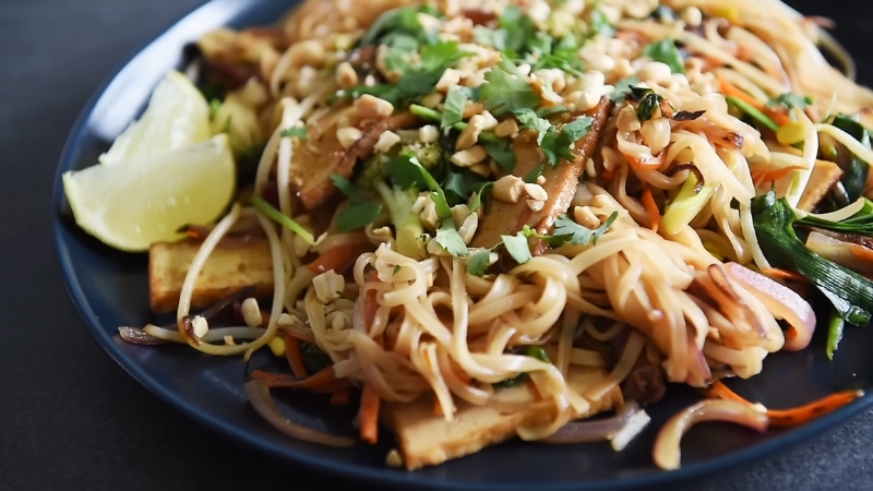 A Plate of Veggie Pad Thai Topped with Chopped Peanuts, Cilantro, and Served with Lime Wedges