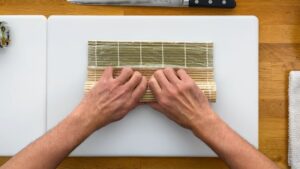 Hands Carefully Rolling Sushi with A Bamboo Mat on A Cutting Board