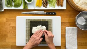 Hands Spreading Sushi Rice Evenly Over a Sheet of Nori Placed on A Bamboo Mat