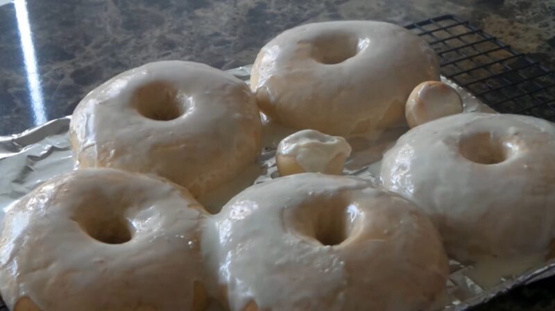 A tray of freshly baked vegan donuts covered in a shiny, translucent classic glaze, cooling on a wire rack