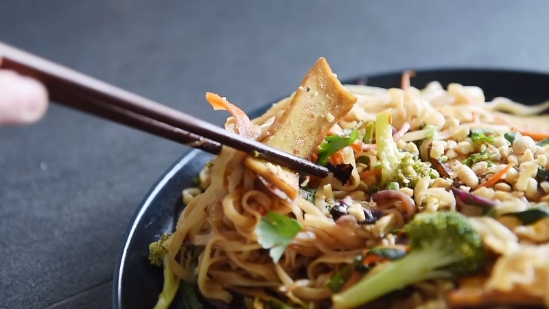 Chopsticks Picking up A Piece of Tofu from A Plate of Freshly Made Veggie Pad Thai