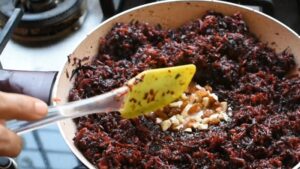 Chopped Nuts Being Added to A Pan of Sautéed Carrot and Beetroot Mixture with A Yellow Spatula