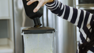 A Person Pouring Olive Oil Into a Running Blender Through the Lid Opening