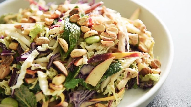 A Bowl of Asian Red Cabbage Salad with Shredded Cabbage, Sliced Apples, Fresh Mint, Edamame, and Crunchy Roasted Peanuts