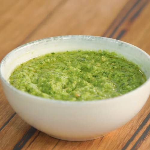 A White Ceramic Bowl Filled with Vibrant Green Broccoli Peanut Pesto Sits on A Wooden Table