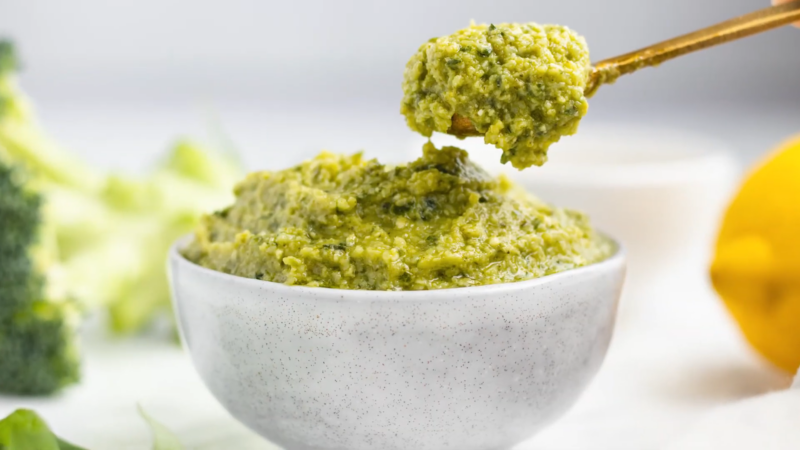 A Spoonful of Broccoli Peanut Pesto Being Lifted from A Speckled White Bowl