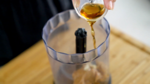 A Hand Pouring a Golden Liquid Into a Food Processor to Prepare the Dressing for Asian Red Cabbage Salad