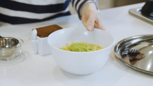 A White Bowl of Spaghetti Topped with Broccoli Peanut Pesto on A Kitchen Counter