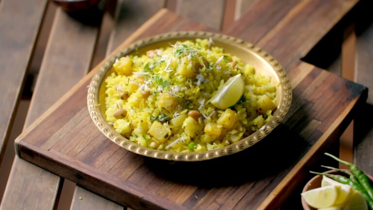 A Plate of Spicy Masala Poha Garnished with Fresh Coriander, Grated Coconut, Roasted Peanuts, and A Wedge of Lime, Served on A Wooden Tray
