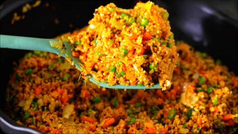 A spoonful of colorful couscous fried “rice” with peas, carrots, and onions in a pan