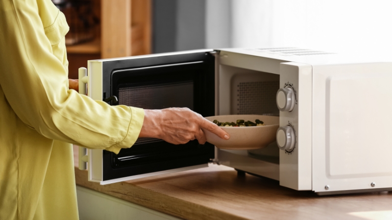A person placing a bowl of food into a microwave