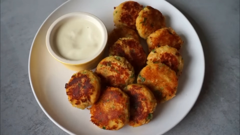 A plate of golden-brown chickpea & sweet potato cutlets served with a small bowl of dipping sauce