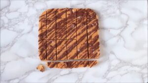 Sliced vegan chocolate peanut butter fudge with a chocolate drizzle sits on a marble surface, ready to serve