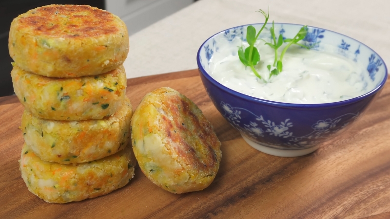A stack of mini chickpea and sweet potato cutlets served on a wooden board with a bowl of creamy dip
