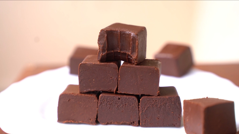 A stack of smooth, square-cut no-bake vegan chocolate peanut butter fudge pieces on a white plate