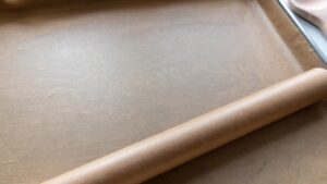 A baking tray lined with parchment paper, with a roll of parchment resting on the edge