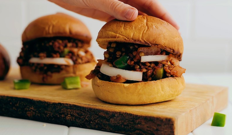 A hand reaches to top a hearty Sloppy Joe sandwich