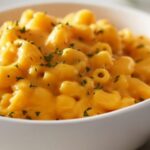 Close-up of creamy, orange macaroni and cheese topped with fresh green parsley in a white bowl