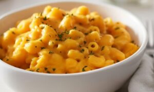 Close-up of creamy, orange macaroni and cheese topped with fresh green parsley in a white bowl