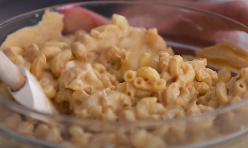 Close-up of velvety cheese sauce coating elbow macaroni noodles during mixing