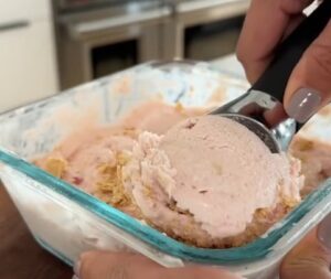 A person scooping ice cream from a tub into a bowl with a metal scoop
