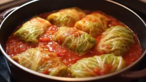 Stuffed cabbage rolls cooking in a pan filled with tomato sauce