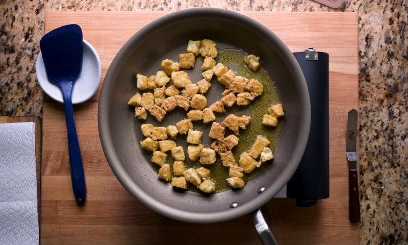 A frying pan filled with tofu pieces, sizzling and ready to serve