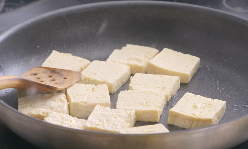 Tofu cubes sizzling in a pan on a stove