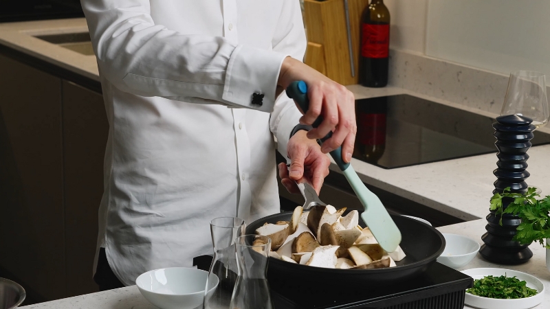 Chef pan sear sliced king oyster mushrooms in a hot skillet on a kitchen counter