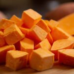 Close up of peeled sweet potato cubes on a wooden cutting board