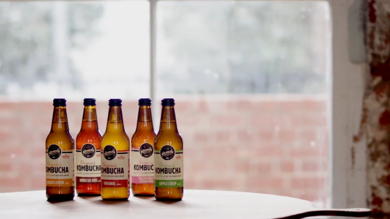 Five bottles of Remedy Kombucha in different flavors on a table by a window