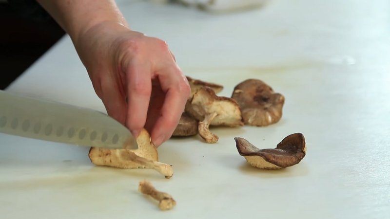 Cook trims shiitake mushroom stems on a cutting board before cooking to avoid tough texture