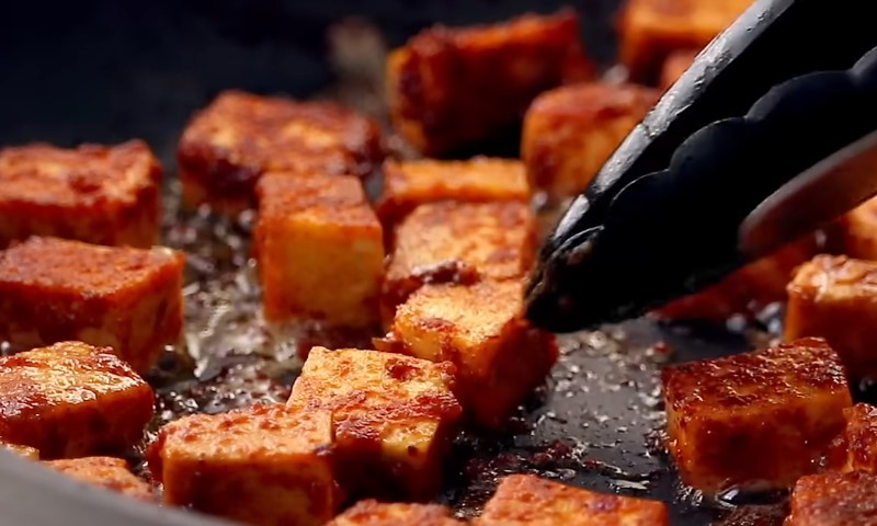A pan with tofu being cooked, showing golden-brown pieces sizzling in oil