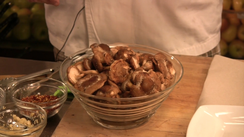 Fresh shiitake mushrooms rest in a bowl on a cutting board before a quick rinse and drying