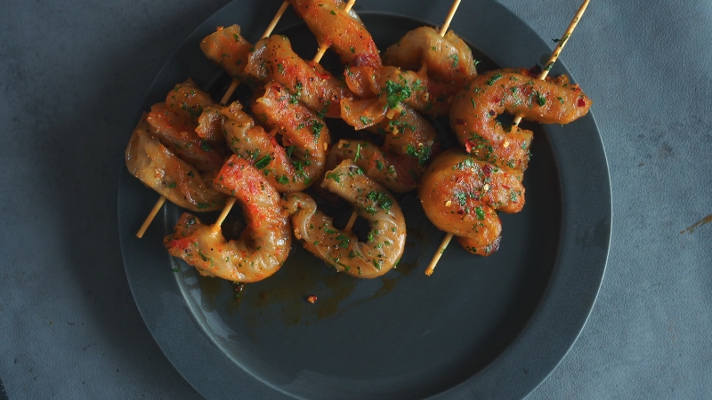 Cooked plant based shrimp skewers on a plate with herbs and light sauce