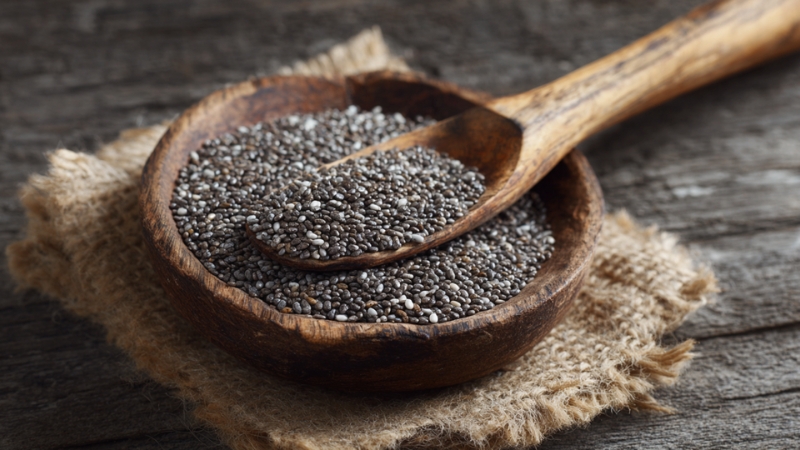 Chia seeds in a wooden bowl with a spoon on a rustic surface