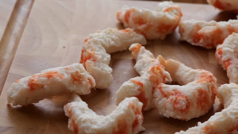 Raw plant based shrimp pieces shaped by hand on a wooden cutting board