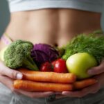 Person holding a variety of vegetables and fruits including carrots, broccoli, tomatoes, and apple