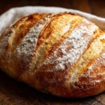 A golden-crusted artisan sourdough loaf dusted with flour on a rustic wooden cutting board